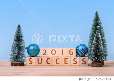 Wooden cubes with numbers 2026 and word success and green Christmas trees on a wooden table and a blue background. New Year 2026 and Christmas postcard. 130577383