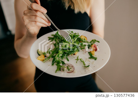 Woman holding plate filled with vibrant, fresh salad featuring arugula, cucumber, peach, and cheese, savoring flavors while embracing healthy lifestyle and nutritious eating habits. Wellness nutrition 130577436