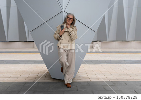 Elegant woman posing casually in modern urban setting with geometric architecture in background 130578229