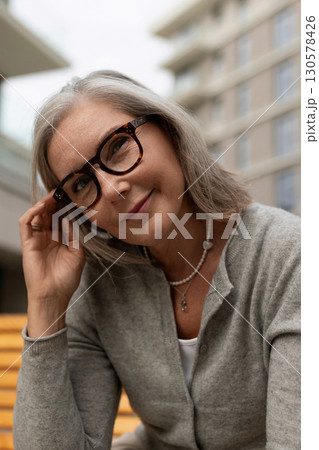 Senior woman smiling while sitting on a wooden bench in a modern urban setting on a cloudy day 130578426