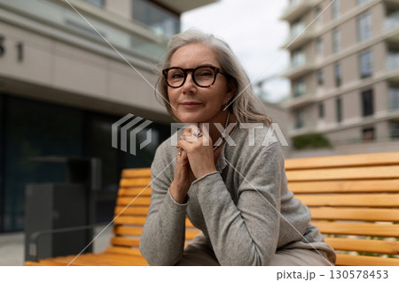 Senior woman enjoys a moment of reflection on a bench in a modern urban setting during a cloudy Senior woman enjoys a moment of reflection on a bench in a modern urban setting during a cloudy 130578453