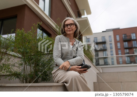 Older woman enjoying a quiet moment on a sunny terrace in the city while holding a smartphone and Older woman enjoying a quiet moment on a sunny terrace in the city while holding a smartphone and 130579074