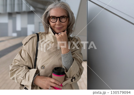 Stylish woman enjoying coffee at urban location in fall afternoon, showcasing modern fashion and 130579094