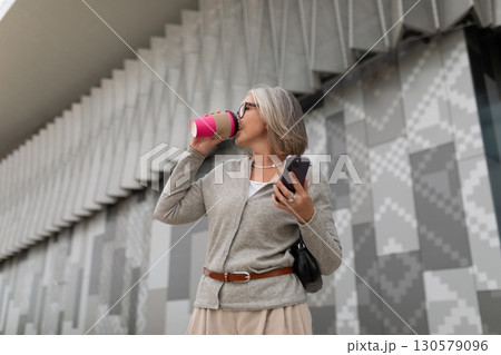 Woman enjoying a coffee while standing outside a modern building showcasing geometric patterns 130579096
