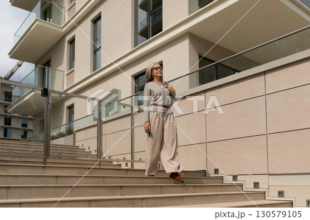Woman walking down the stairs of a modern building wearing light clothing and stylish glasses in the Woman walking down the stairs of a modern building wearing light clothing and stylish glasses in the 130579105