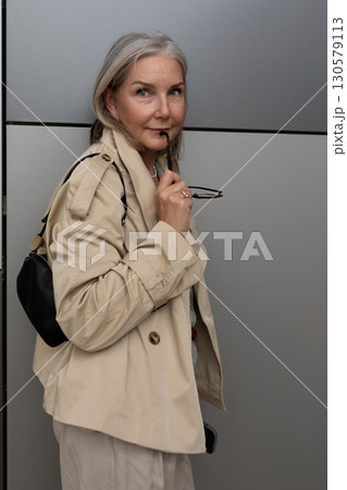Elegant woman in neutral outfit poses against a modern backdrop while holding sunglasses with Elegant woman in neutral outfit poses against a modern backdrop while holding sunglasses with 130579113