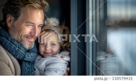 Loving father embraces smiling daughter with the magic of winter reflected in the window. Loving father embraces smiling daughter with the magic of winter reflected in the window. 130579415