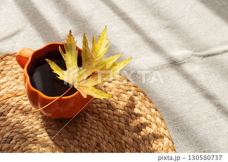 Pumpkin Mug with Coffee and Autumn Leaf on Woven Placemat 130580737