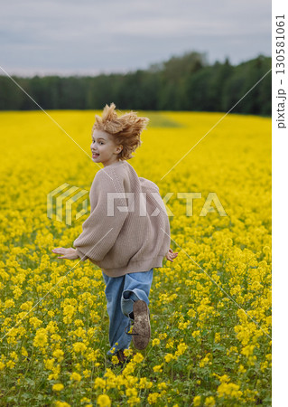Smiling girl in beige sweater running in yellow flower field looking at camera Smiling girl in beige sweater running in yellow flower field looking at camera 130581061