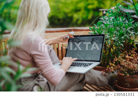 Mature woman sitting on balcony with laptop, working remotely. Mature woman sitting on balcony with laptop, working remotely. 130581331