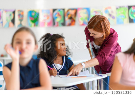 Teacher talking with school girl, children in primary class. 130581336