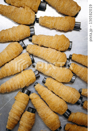 Raw puff pastry tubes for cream rolls on metal tray in bakery kitchen 130582019