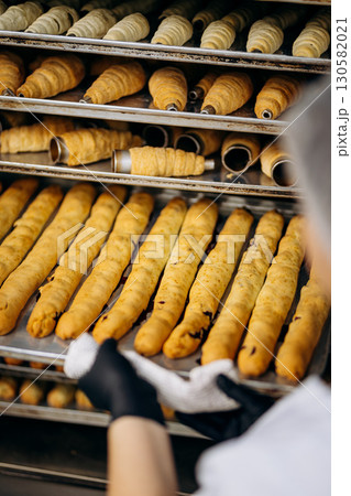 Freshly baked pastry tubes and rolls on industrial trays in bakery kitchen 130582021