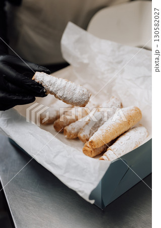 Freshly baked cream horns in powdered sugar held in hand over pastry box 130582027