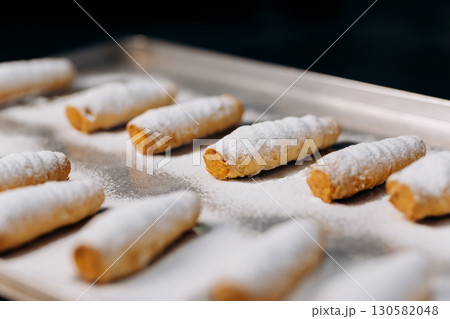 Freshly baked cream rolls sprinkled with powdered sugar on a metal tray in bakery 130582048