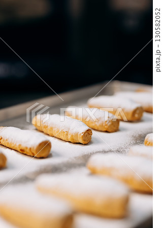 Freshly baked cream rolls sprinkled with powdered sugar on a metal tray in bakery Freshly baked cream rolls sprinkled with powdered sugar on a metal tray in bakery 130582052