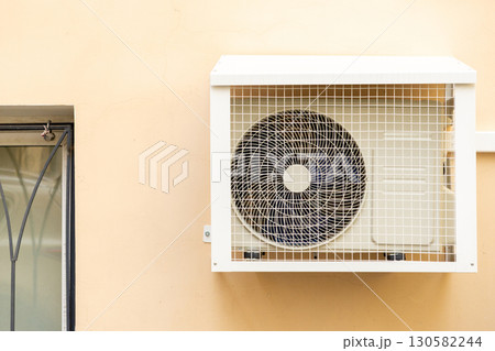 air conditioner in an anti-vandal grid is installed on wall of house.  130582244