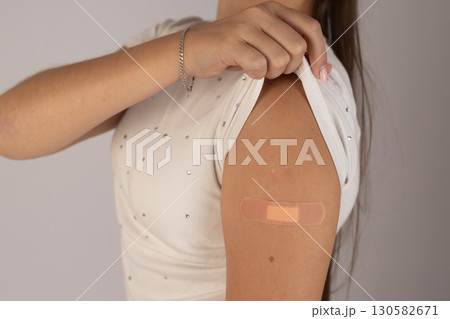 Woman is lifting her sleeve to reveal a bandage on her upper arm, indicating  130582671