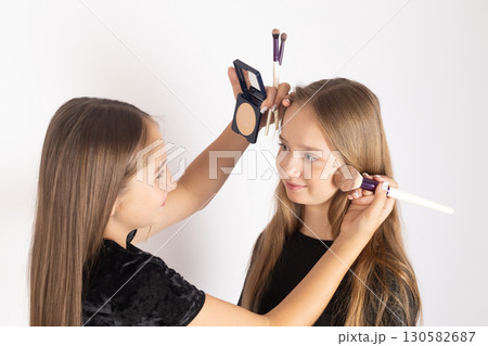 One girl is applying makeup to another girl's face using a brush and a compact 130582687