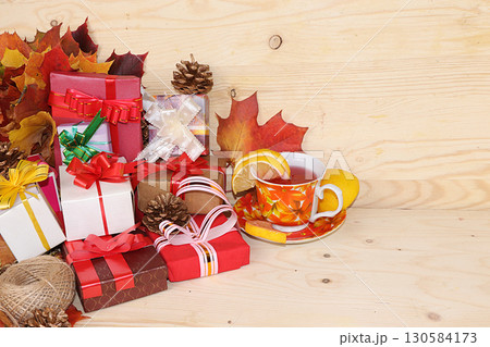 Thanksgiving, autumn background with seasonal maple leaves, a cup of hot tea with lemon and gifts on a wooden background, copy space, preparation for the holiday. Happy Thanksgiving concept, 130584173