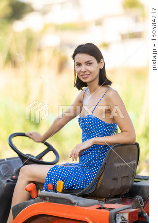 Young woman sits on minitractor and drives rural vehicle, performs loading work on farm 130584217