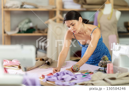Young female seamstress attaching template to fabric Young female seamstress attaching template to fabric 130584246