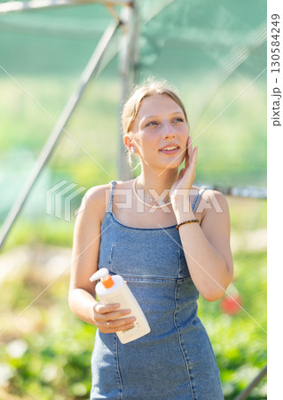 Young woman applying sunscreen in garden greenhouse Young woman applying sunscreen in garden greenhouse 130584249
