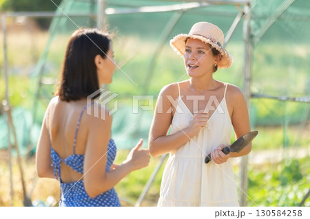 Two women talking in garden greenhouse Two women talking in garden greenhouse 130584258