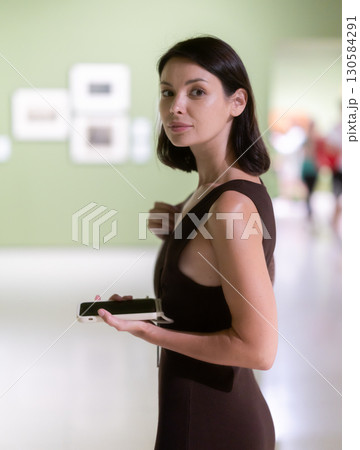 Woman with phone in hands in museum hall, view painting exhibition Woman with phone in hands in museum hall, view painting exhibition 130584291