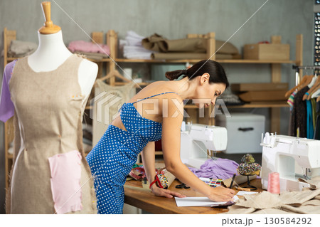 Young woman seamstress draws sketch on paper Young woman seamstress draws sketch on paper 130584292