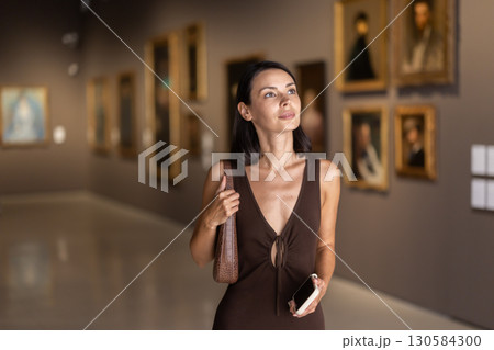 Woman visiting museum and looking at paintings in gold frames 130584300