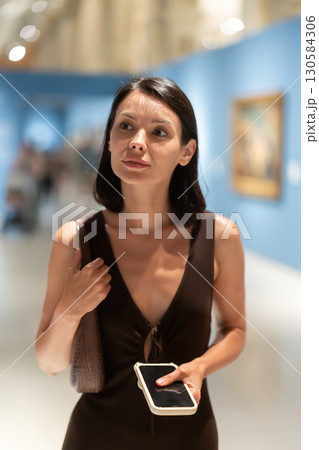 Woman with phone in hands in museum hall, view painting exhibition Woman with phone in hands in museum hall, view painting exhibition 130584306