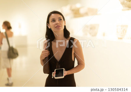 Girl spends time in museum, examines European antique heritage, hall with columns 130584314