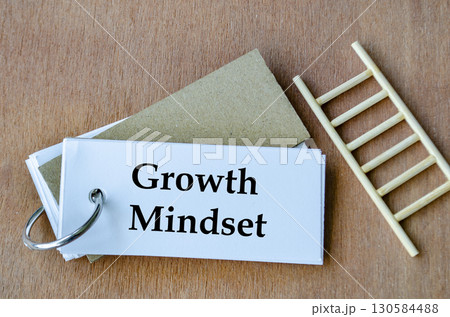 Notepad beside miniature ladder displaying Growth Mindset handwritten neatly in black. Notepad beside miniature ladder displaying Growth Mindset handwritten neatly in black. 130584488