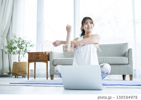 自宅でパソコンを見ながらストレッチする若い女性 自宅でパソコンを見ながらストレッチする若い女性 130584978