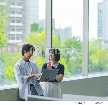窓際で会話する大学生男女とノートPC 窓際で会話する大学生男女とノートPC 130585055
