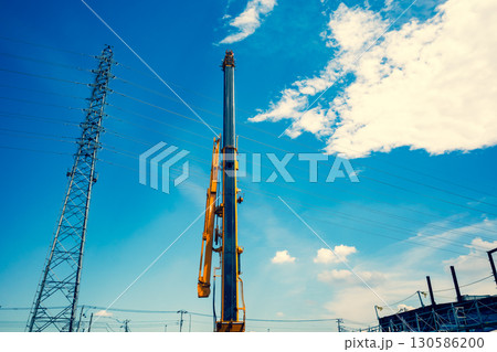 空に伸びるクレーンのアームと送電鉄塔　c-3 暖色寒色強調 130586200