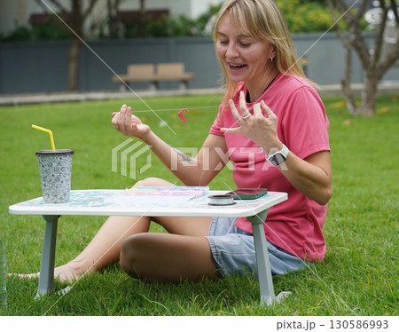 Young woman beading colorful bracelets outdoors in a park Young woman beading colorful bracelets outdoors in a park 130586993