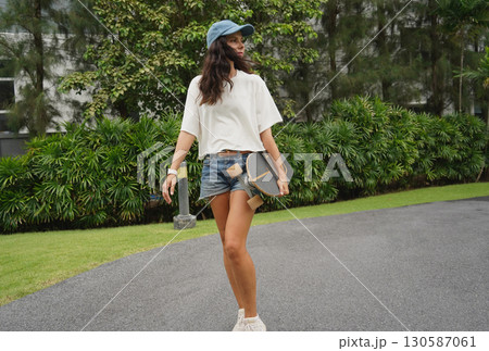 A woman is walking at the city park while carrying a skateboard in her hands 130587061
