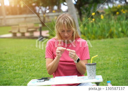 Young woman beading colorful bracelets outdoors in a park 130587137