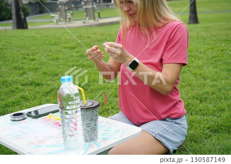 Young woman beading colorful bracelets outdoors in a park Young woman beading colorful bracelets outdoors in a park 130587149