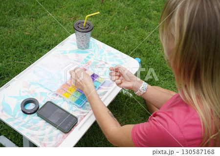 Young woman beading colorful bracelets outdoors in a park 130587168