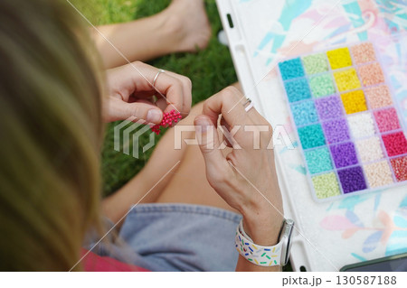 Young woman beading colorful bracelets outdoors in a park Young woman beading colorful bracelets outdoors in a park 130587188