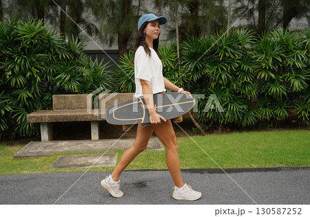 A woman is walking at the city park while carrying a skateboard in her hands 130587252
