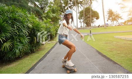 A young woman is skillfully riding a skateboard down a scenic park 130587255