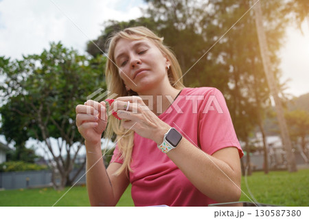 Young woman beading colorful bracelets outdoors in a park Young woman beading colorful bracelets outdoors in a park 130587380