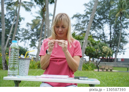 Young woman beading colorful bracelets outdoors in a park 130587393