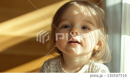 Joyful toddler with bright eyes and soft hair enjoying sunlight indoors 130587510