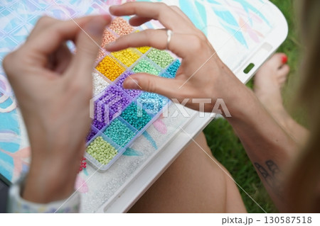 Young woman beading colorful bracelets outdoors in a park Young woman beading colorful bracelets outdoors in a park 130587518