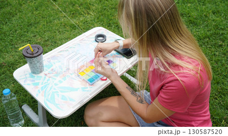 Young woman beading colorful bracelets outdoors in a park Young woman beading colorful bracelets outdoors in a park 130587520